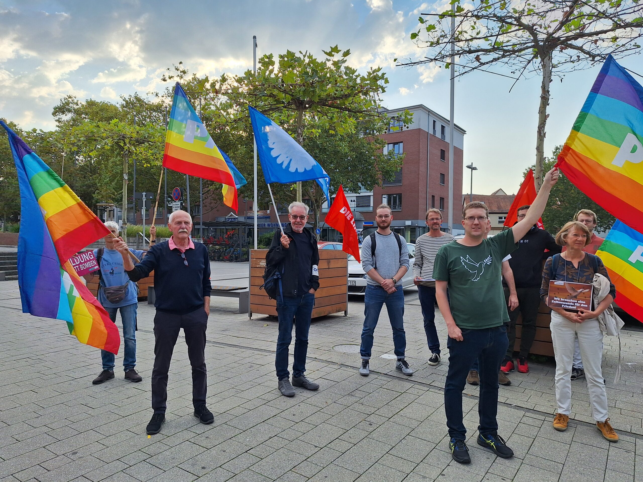 15 Menschen stehen mit bunten Friedensfahnen auf dem Chinonplatz in Hofheim