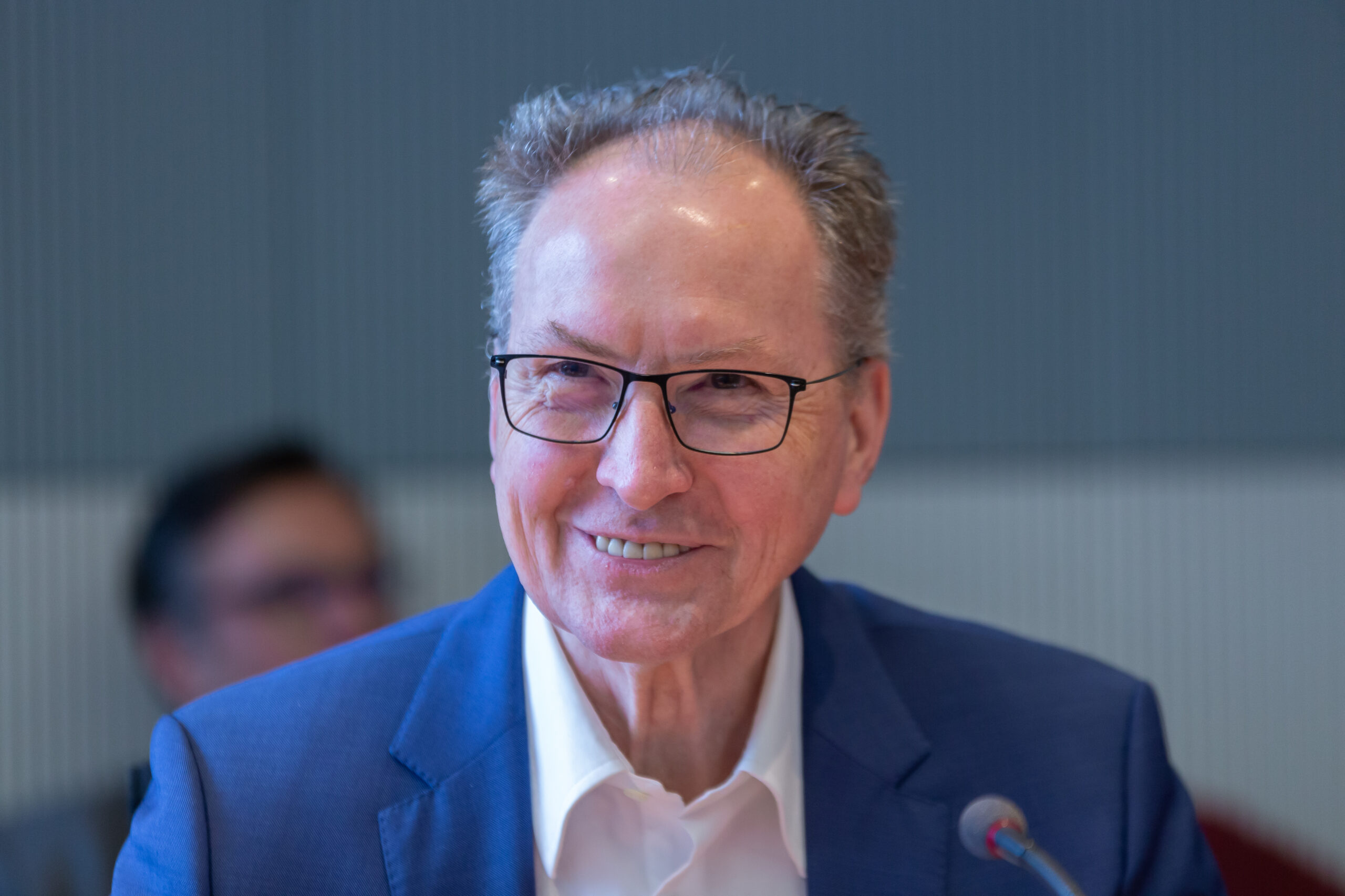 Ein älterer lächelnder Herr mit Brille und Halbglatze und blauem Anzug