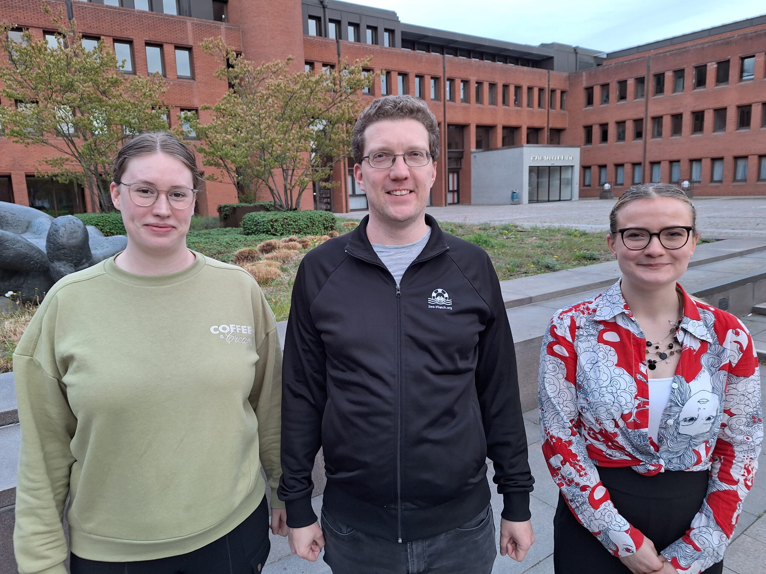 Zwei Frauen und ein Mann stehen im Innenhof eines Backsteingebäudes