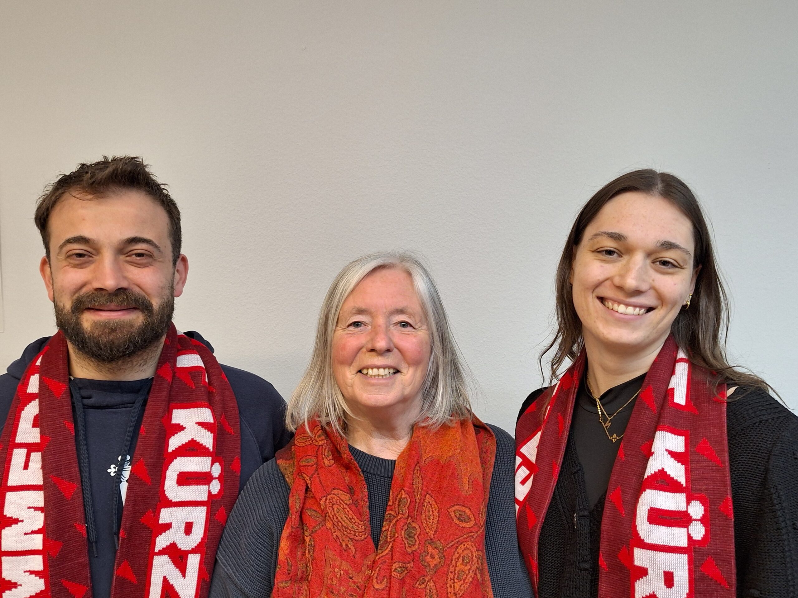 Zwei Frauen und ein Mann alle mit roten Schals oder Halstüchern bekleidet